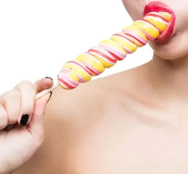 A woman practicing blowjob techniques with a long lollipop in her mouth