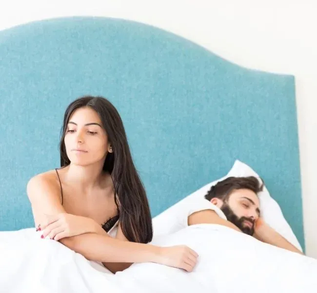 Ein entspannt schlafender Mann  und eine Frau die wach im Bett neben ihm sitzt